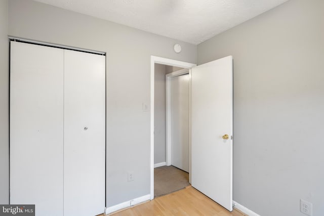 unfurnished bedroom featuring a textured ceiling, a closet, and light wood-type flooring