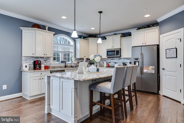 kitchen featuring light stone counters, stainless steel appliances, a kitchen island, decorative light fixtures, and crown molding