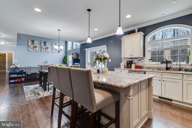 kitchen with a center island, pendant lighting, white cabinets, a sink, and light stone countertops