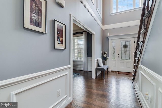 foyer entrance with dark wood-style floors, wainscoting, and a high ceiling