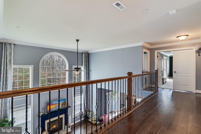 hallway with dark wood-style floors, baseboards, visible vents, and ornamental molding