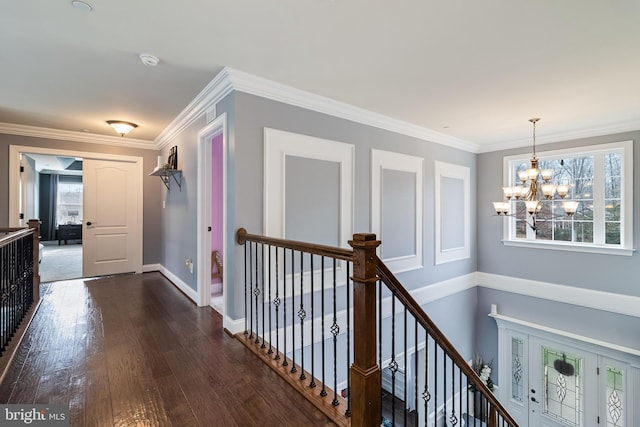 hall featuring a notable chandelier, dark wood-type flooring, an upstairs landing, baseboards, and ornamental molding