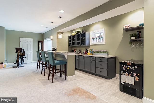 bar with baseboards, light carpet, hanging light fixtures, and a bar