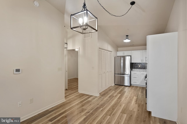 kitchen with stainless steel fridge, vaulted ceiling, decorative light fixtures, a chandelier, and white cabinetry