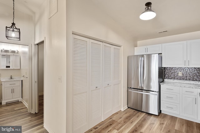 kitchen with stainless steel refrigerator, white cabinets, pendant lighting, and light wood-type flooring