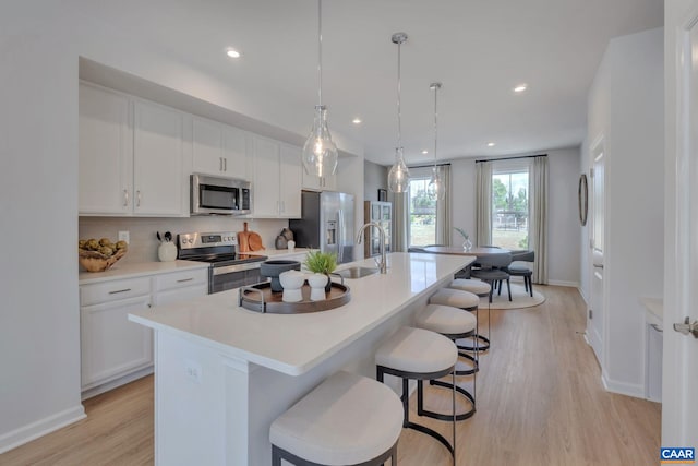 kitchen with white cabinets, decorative light fixtures, stainless steel appliances, and a kitchen island with sink