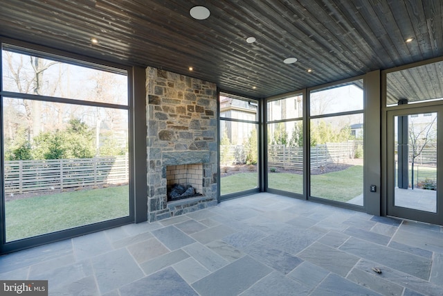 unfurnished sunroom with an outdoor stone fireplace, wooden ceiling, and a wealth of natural light