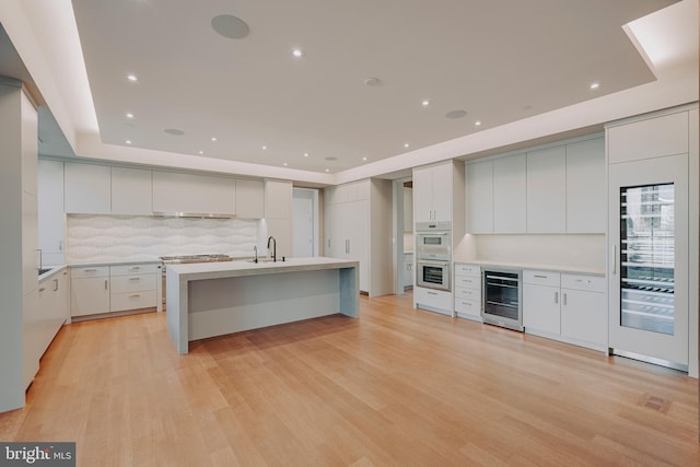 kitchen with sink, wine cooler, backsplash, light hardwood / wood-style floors, and white cabinets