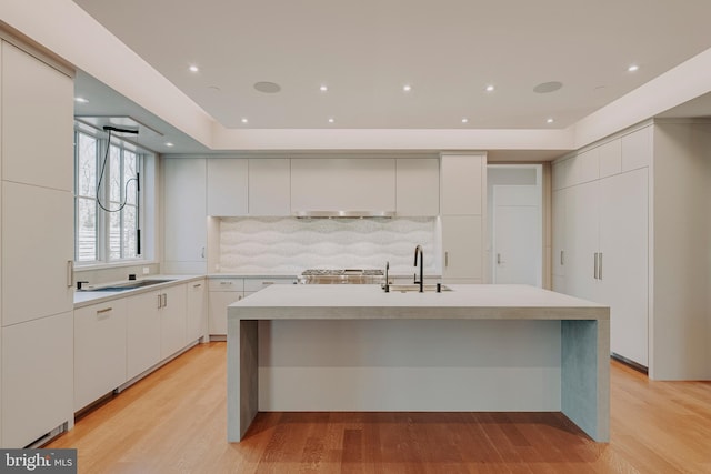 kitchen featuring tasteful backsplash, a kitchen island with sink, sink, light hardwood / wood-style flooring, and white cabinets