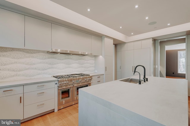 kitchen featuring exhaust hood, range with two ovens, sink, decorative backsplash, and an island with sink