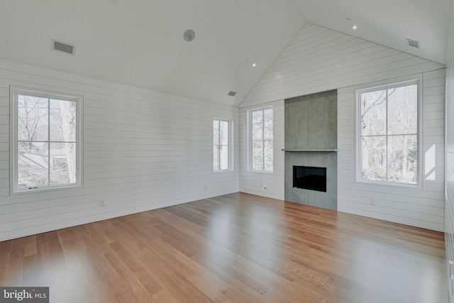 unfurnished living room with wood walls, a fireplace, high vaulted ceiling, and light hardwood / wood-style floors