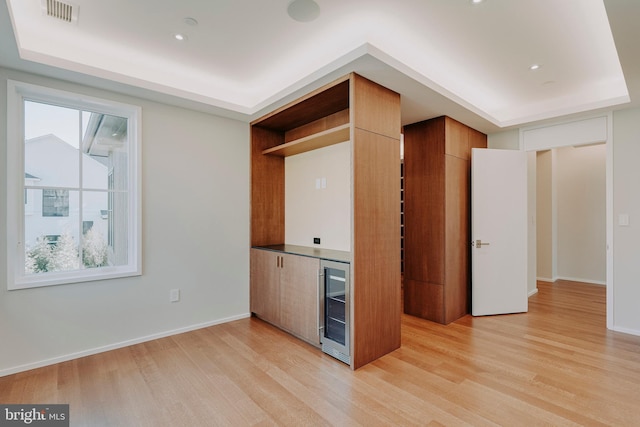 kitchen with a tray ceiling, light hardwood / wood-style flooring, and beverage cooler