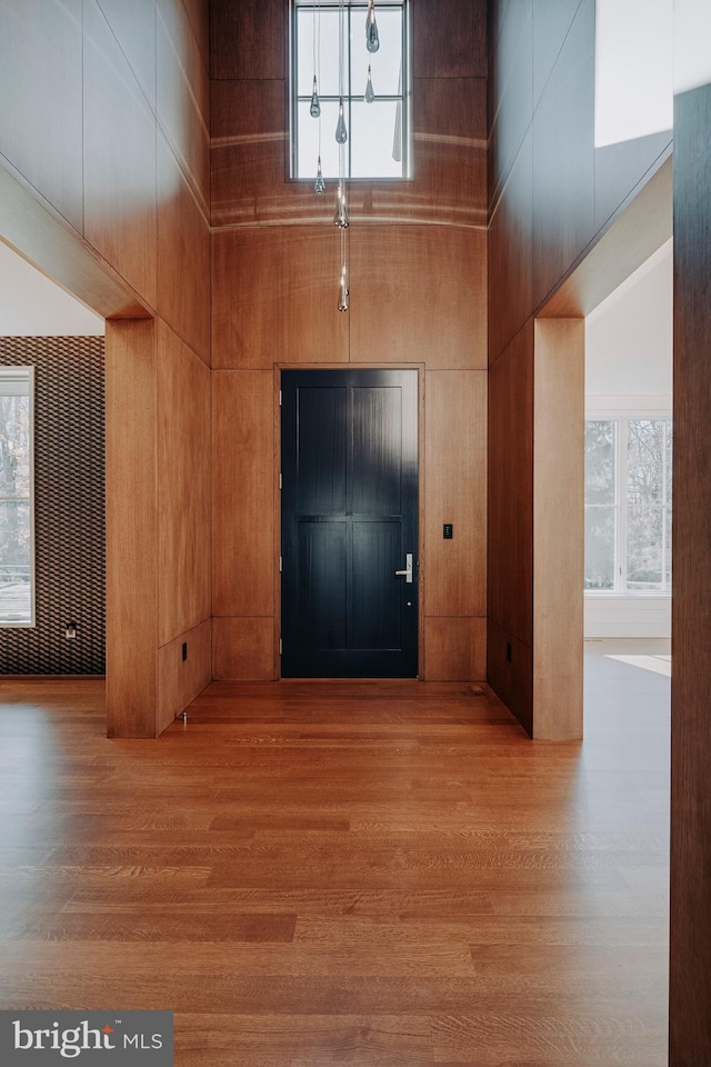 foyer featuring a towering ceiling, light hardwood / wood-style flooring, and wood walls