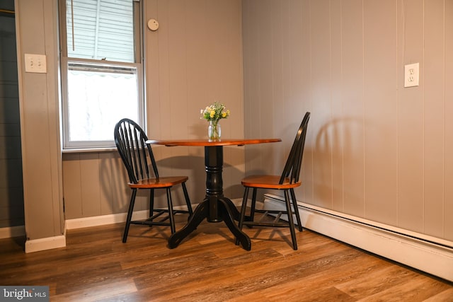 dining space featuring hardwood / wood-style floors, a baseboard heating unit, and wood walls