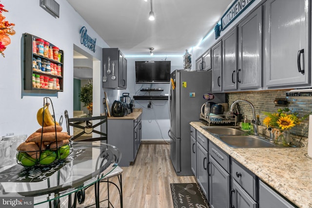 kitchen with gray cabinetry, sink, backsplash, stainless steel fridge, and light wood-type flooring