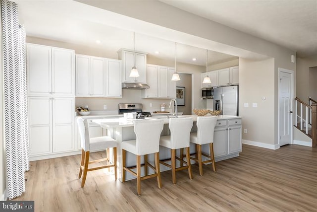 kitchen featuring white cabinets, appliances with stainless steel finishes, light hardwood / wood-style floors, and a kitchen island with sink