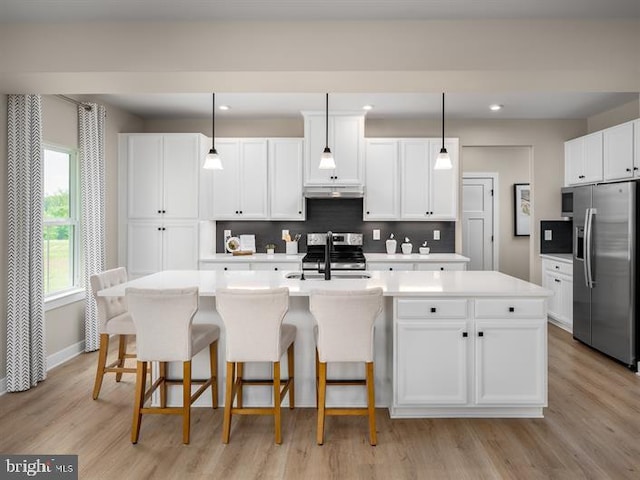 kitchen with sink, hanging light fixtures, appliances with stainless steel finishes, and an island with sink