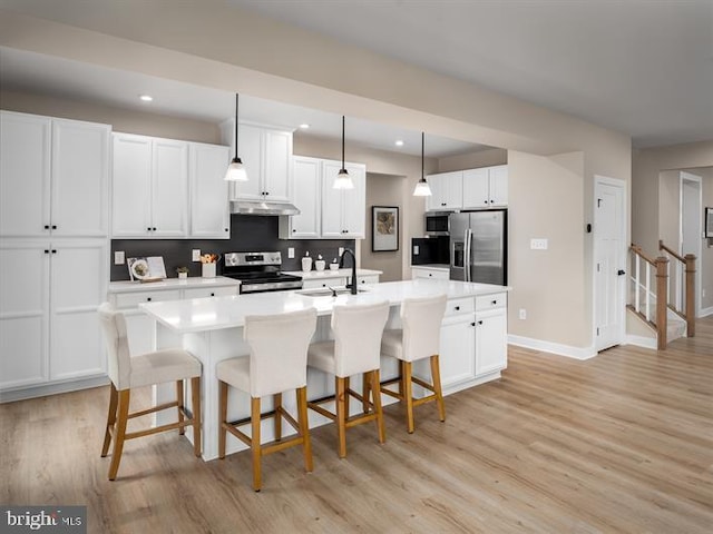 kitchen featuring white cabinetry, light hardwood / wood-style flooring, decorative light fixtures, a kitchen island with sink, and appliances with stainless steel finishes