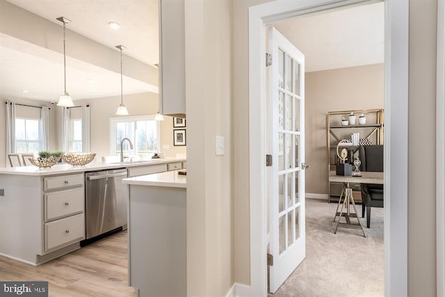 kitchen featuring stainless steel dishwasher, sink, pendant lighting, white cabinets, and light hardwood / wood-style floors