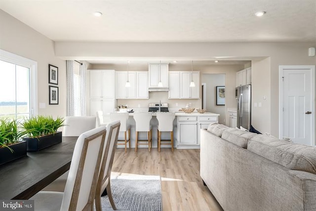 kitchen featuring a kitchen breakfast bar, white cabinetry, stainless steel refrigerator, and light hardwood / wood-style flooring