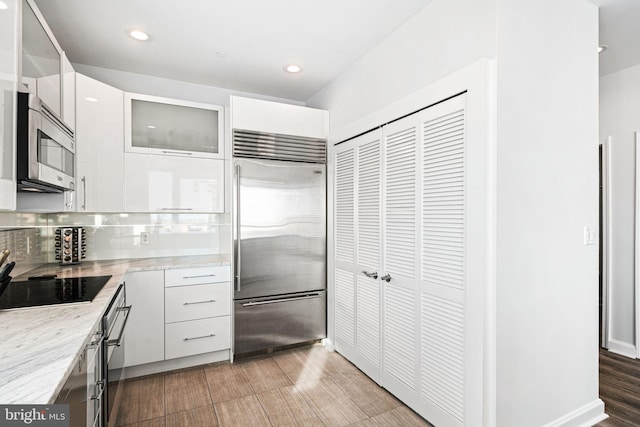 kitchen with decorative backsplash, light wood-type flooring, appliances with stainless steel finishes, light stone counters, and white cabinetry