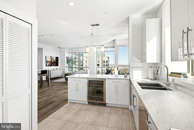 kitchen with white cabinetry, sink, rail lighting, and beverage cooler