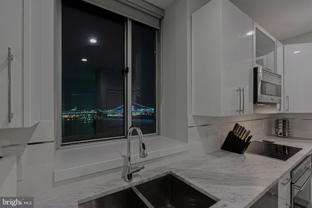 kitchen with light stone countertops, white cabinetry, sink, and stainless steel appliances