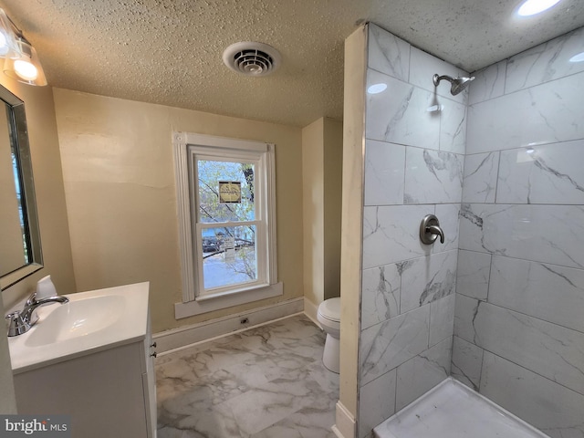 bathroom with a tile shower, vanity, a textured ceiling, and toilet