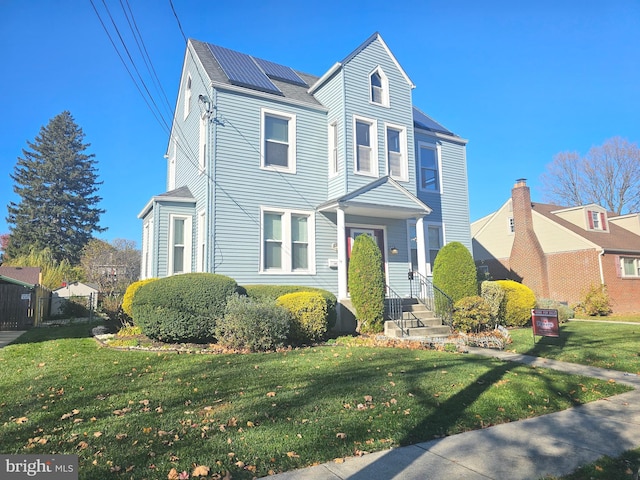 view of property featuring a front yard and solar panels