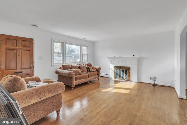 living room featuring a tiled fireplace, light hardwood / wood-style floors, and a baseboard radiator