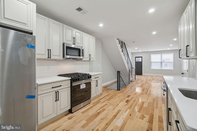 kitchen featuring white cabinets, light wood-type flooring, backsplash, and appliances with stainless steel finishes