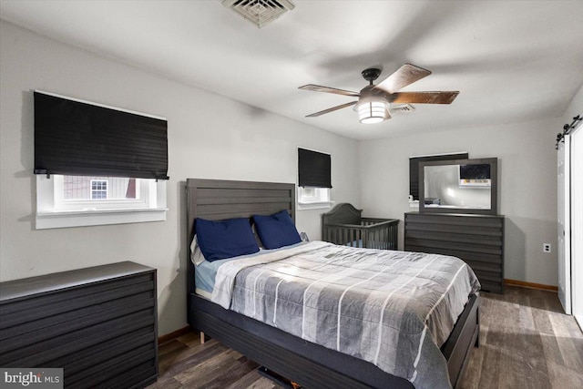 bedroom with dark hardwood / wood-style flooring, ceiling fan, and a barn door