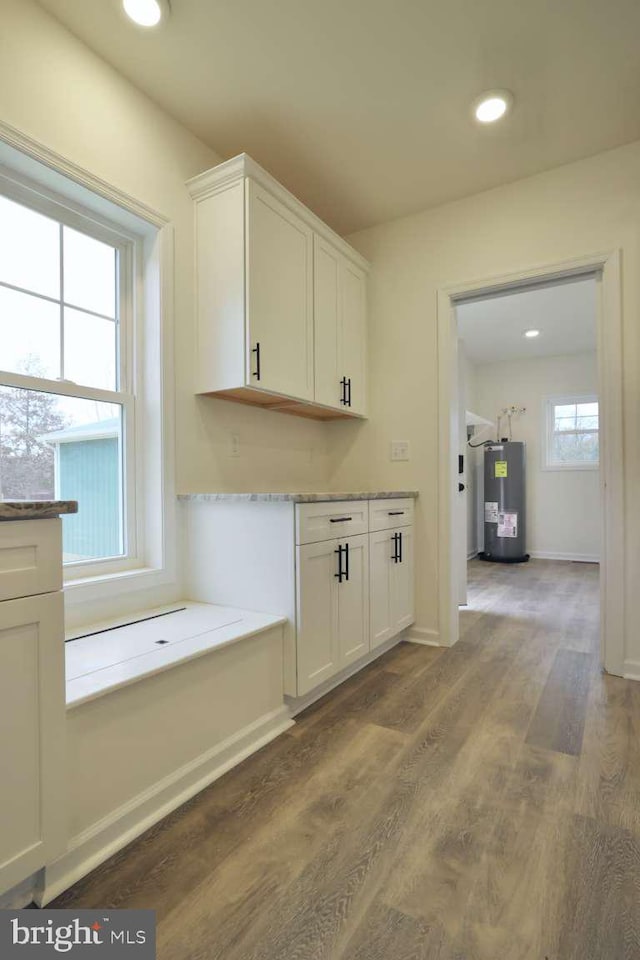 kitchen featuring electric water heater, white cabinetry, dark wood-type flooring, and a wealth of natural light