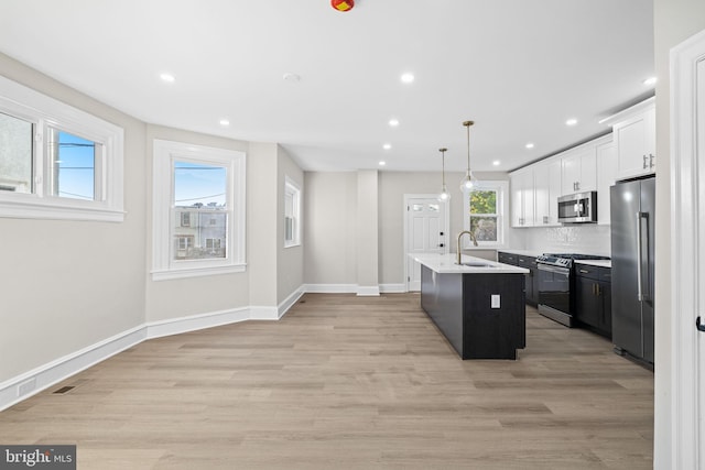 kitchen with pendant lighting, white cabinets, an island with sink, light hardwood / wood-style floors, and stainless steel appliances