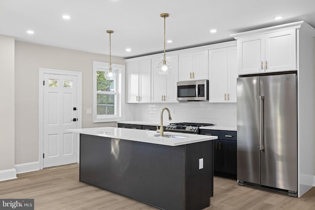 kitchen featuring a center island with sink, white cabinets, pendant lighting, and appliances with stainless steel finishes