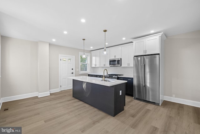 kitchen with white cabinetry, hanging light fixtures, an island with sink, and stainless steel appliances