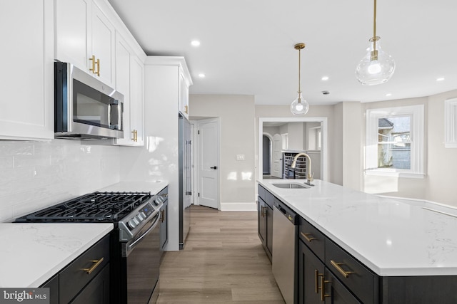 kitchen with light wood-type flooring, stainless steel appliances, sink, pendant lighting, and white cabinets