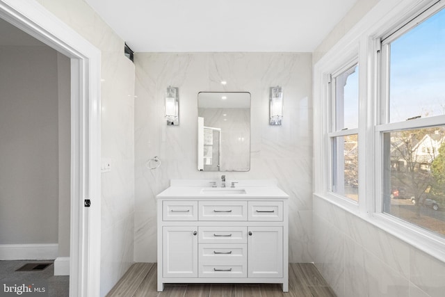 bathroom with vanity, a healthy amount of sunlight, tile walls, and hardwood / wood-style flooring