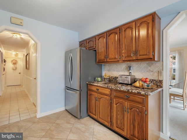 kitchen featuring light tile patterned floors, tasteful backsplash, stainless steel refrigerator, and dark stone countertops