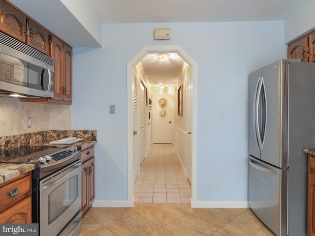 kitchen with dark stone countertops, decorative backsplash, light tile patterned floors, and appliances with stainless steel finishes