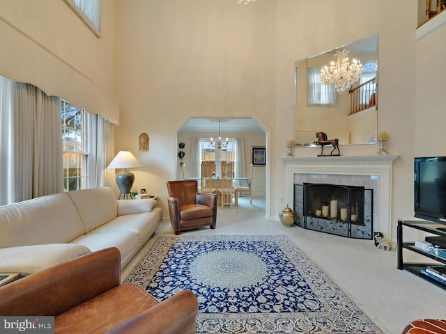 carpeted living room with a premium fireplace, plenty of natural light, a high ceiling, and a notable chandelier