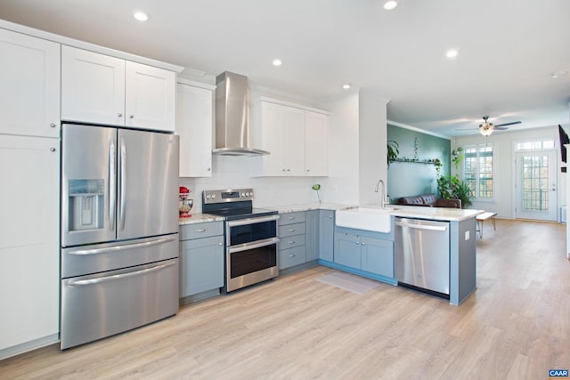 kitchen featuring white cabinets, sink, wall chimney exhaust hood, appliances with stainless steel finishes, and kitchen peninsula