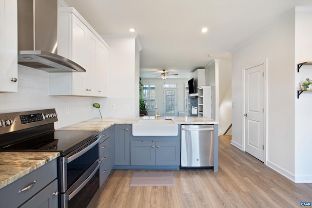 kitchen with ceiling fan, wall chimney exhaust hood, light hardwood / wood-style flooring, white cabinets, and appliances with stainless steel finishes