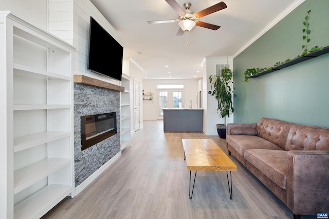 living room featuring crown molding, light hardwood / wood-style flooring, built in shelves, ceiling fan, and a fireplace