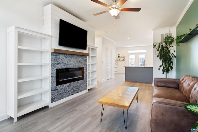 living room with hardwood / wood-style floors, ceiling fan, a stone fireplace, and crown molding