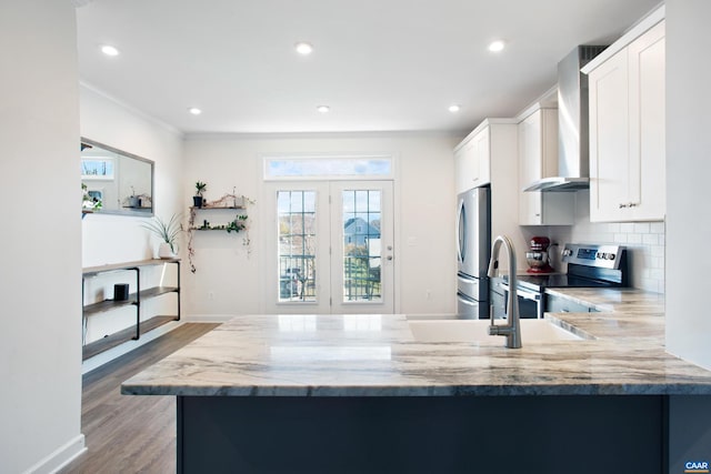 kitchen featuring white cabinetry, wall chimney range hood, kitchen peninsula, hardwood / wood-style floors, and appliances with stainless steel finishes