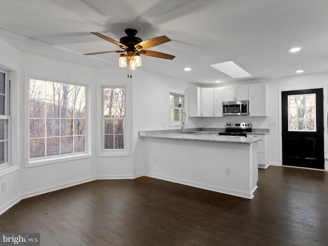 kitchen featuring white cabinets, appliances with stainless steel finishes, light stone countertops, and a wealth of natural light