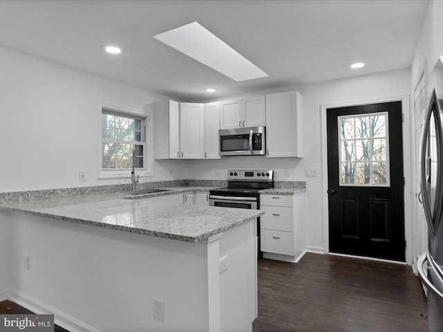 kitchen with kitchen peninsula, appliances with stainless steel finishes, white cabinetry, and a healthy amount of sunlight