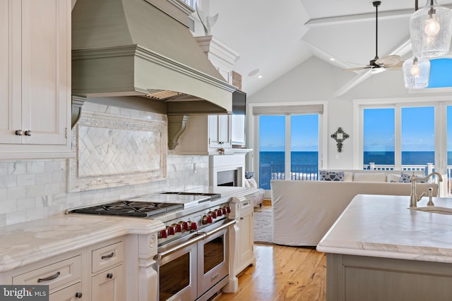 kitchen featuring light hardwood / wood-style floors, decorative light fixtures, range with two ovens, a water view, and custom range hood