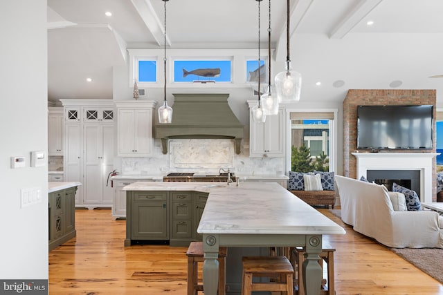 kitchen with decorative light fixtures, beam ceiling, custom range hood, and light hardwood / wood-style flooring